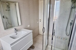 Un baño con lavamanos blanco, cabina de ducha con mampara de vidrio y espejo.