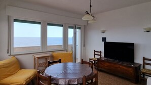 A living room with a round table, yellow sofa, TV, and large windows with a view of the sea. - P012 - Porto Recanati, wonderful three-room apartment facing the sea (Porto Recanati)
