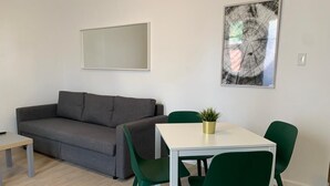 En moderne stue med en grå sofa, et hvidt bord og grønne stole. Et indrammet kunstværk hænger på væggen, og der står en lille plante på bordet.