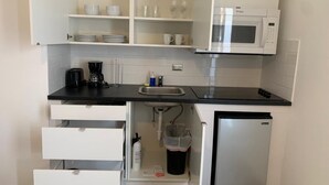 Et lille køkken med hvide skabe, en sort bordplade, en indbygget mikrobølgeovn og et lille køleskab.
