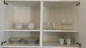 En hvid reol med hvide skåle, tallerkener, glas og krus.
