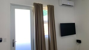 Et værelse med en hvid dør, beige gardiner, et ophængt TV og en aircondition.