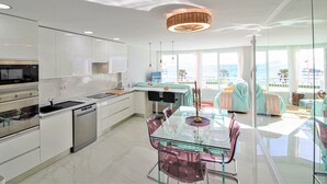 Una cocina moderna con mesa y sillas de vidrio, electrodomésticos de acero inoxidable y vistas al mar a través de grandes ventanales.