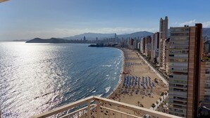Paisagem costeira com praia, edifícios altos e céu claro.