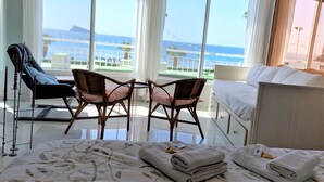 Una habitación de hotel con una cama, dos sillones de mimbre, una mesa y vista al océano.