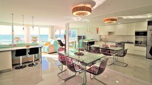 Una cocina moderna con una mesa de comedor de vidrio, electrodomésticos de acero inoxidable y vista al océano.
