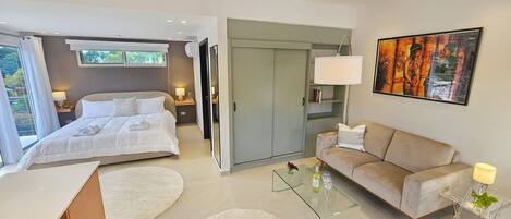 Una habitación de hotel moderna con una cama, un sofá, una mesa de centro de vidrio y un cuadro en la pared.