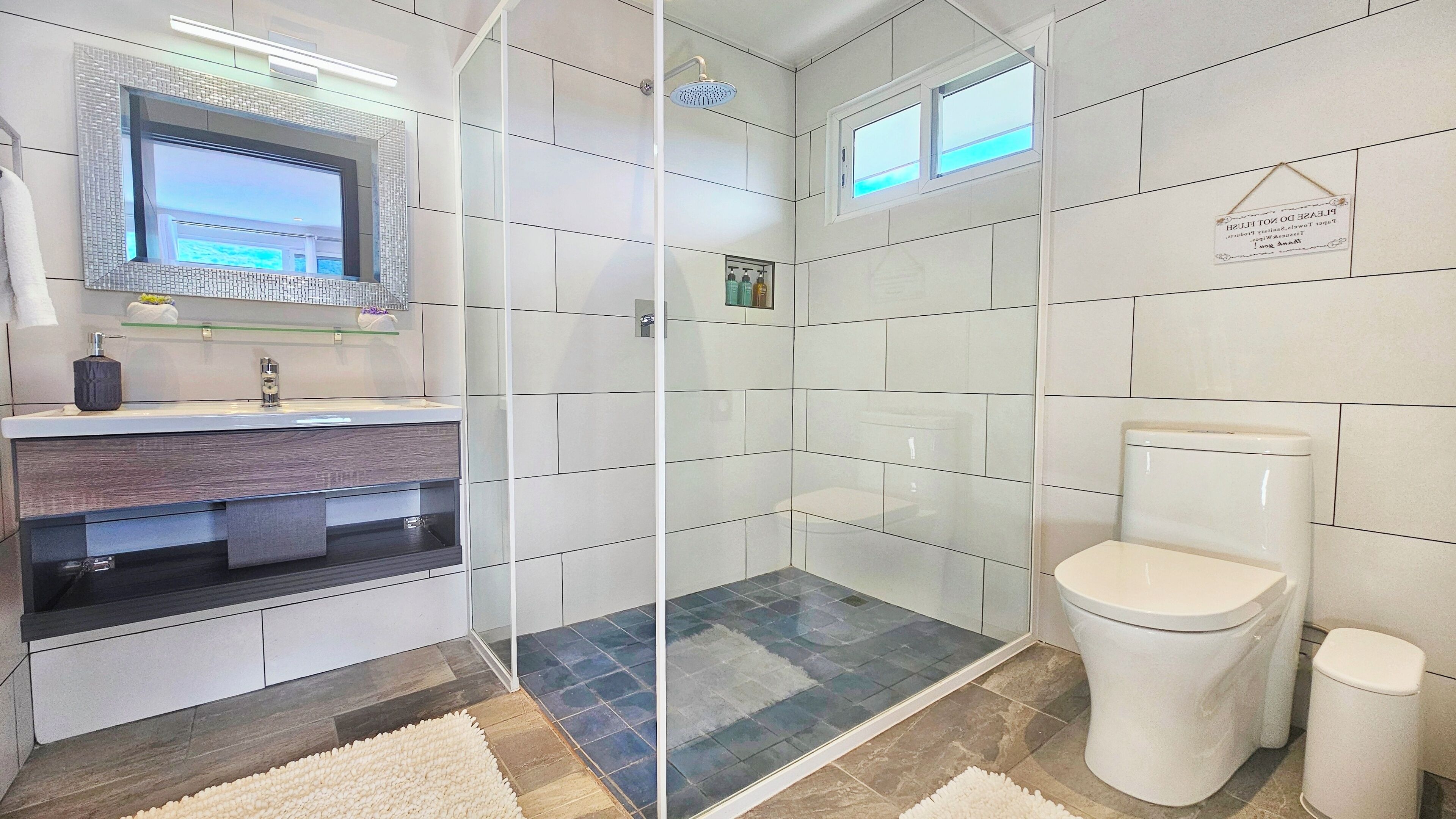 Ein modernes Badezimmer mit Glasdusche, Toilette und Waschtisch mit Spiegel.