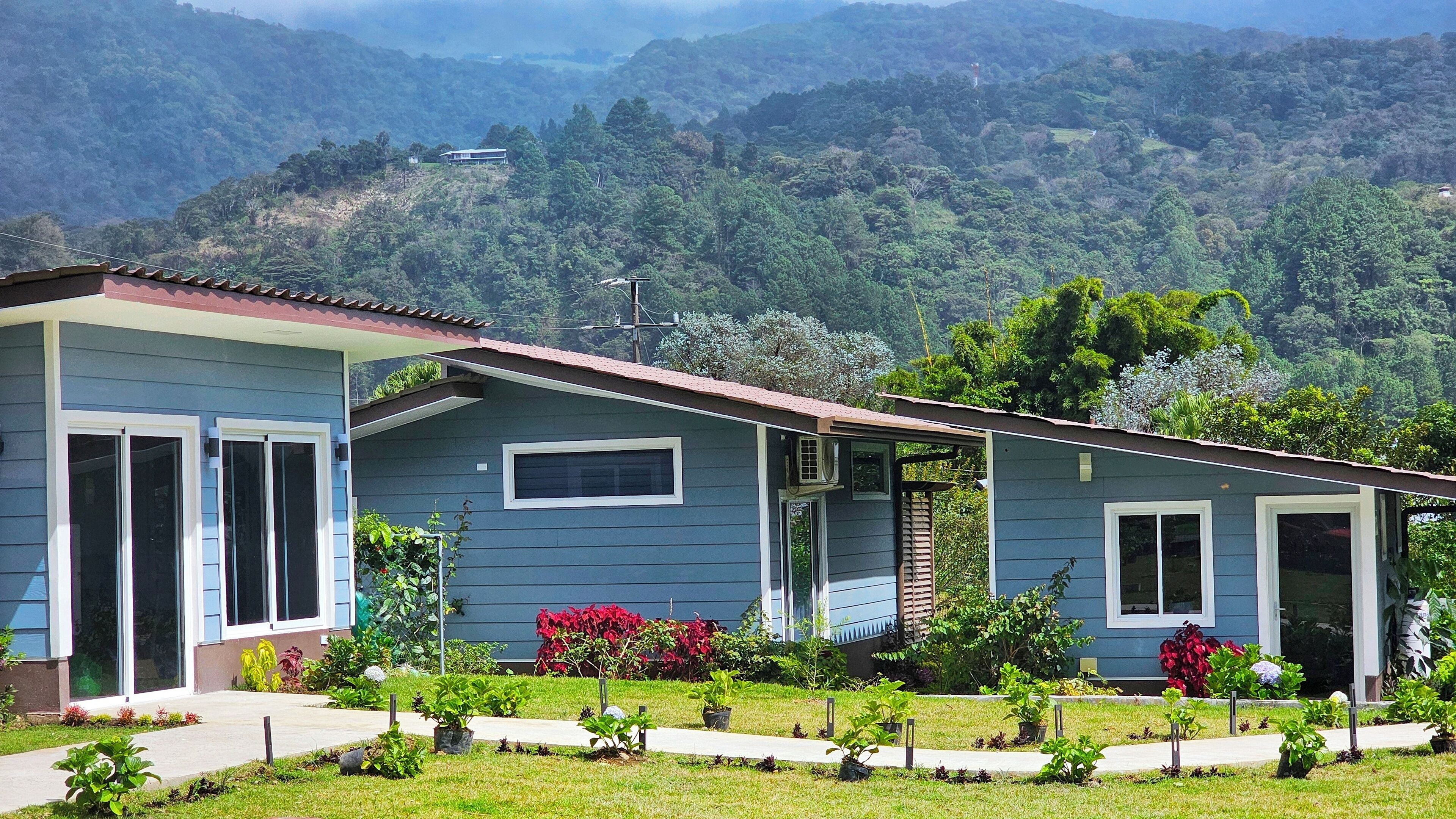 Una casa de dos pisos con techo rojo, rodeada de un jardín bien cuidado con diversas plantas y flores.
