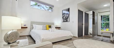 A modern bedroom with a large bed, bedside tables, a chair, and a view of the outdoors.
