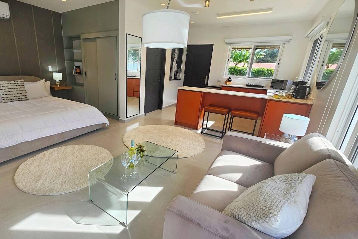 A modern bedroom with a large bed, a glass coffee table, a sofa, and a kitchen area with a bar.