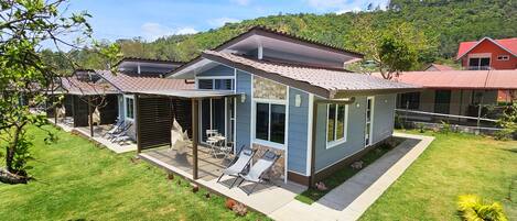 A modern house with a patio, a covered seating area, and a view of a lush green hillside.