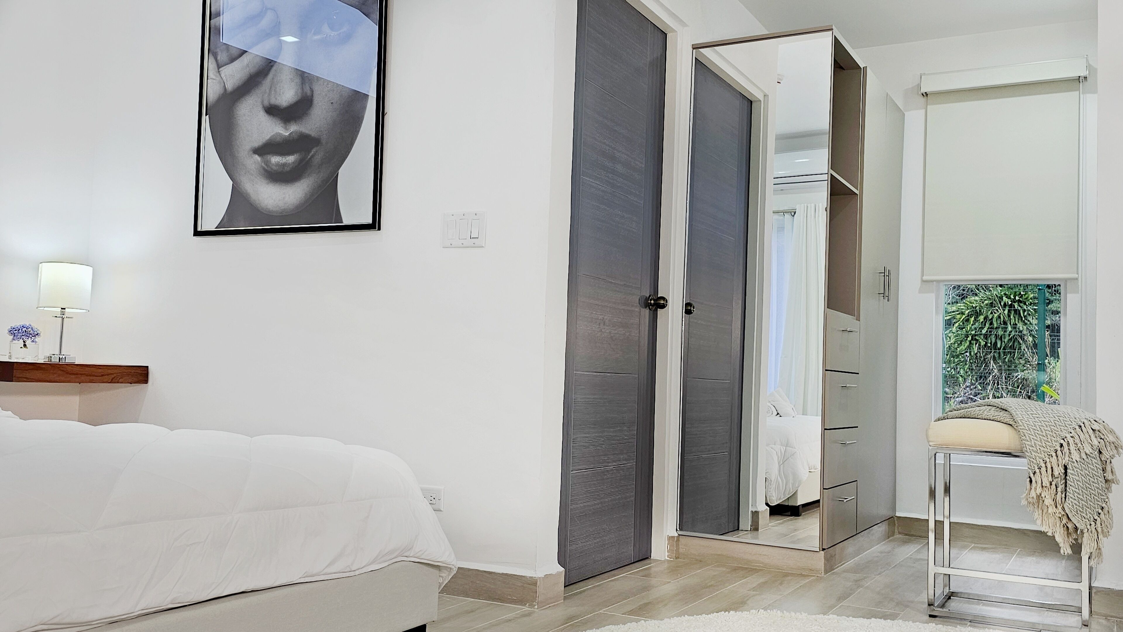 A bedroom with a bed, a wardrobe, a mirror, and a door leading to another room.