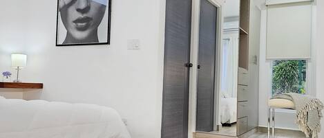A bedroom with a bed, a wardrobe, a mirror, and a door leading to another room.