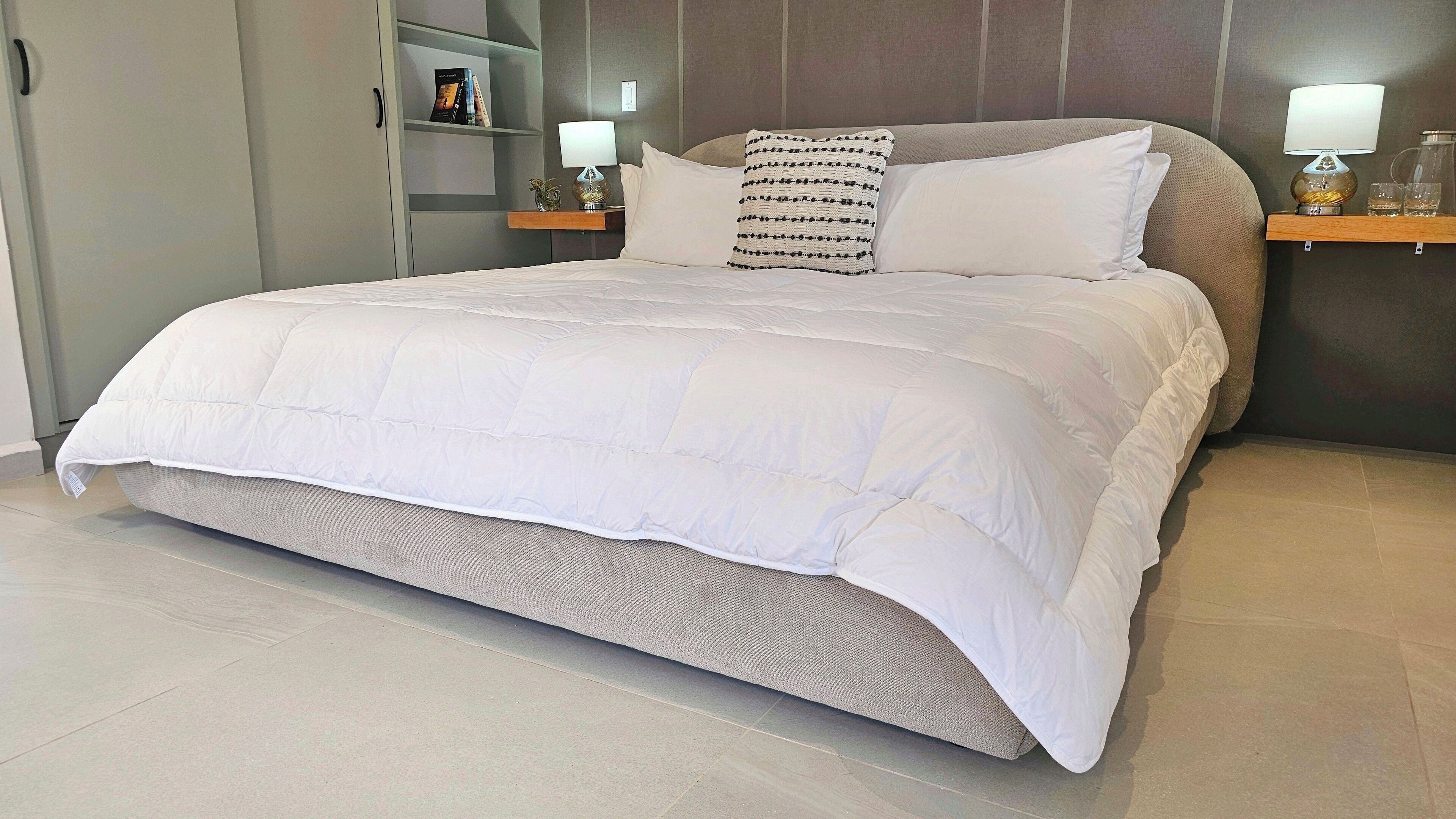 A neatly made bed with a white duvet, a grey headboard, and a bedside table with a lamp and a small decorative item.