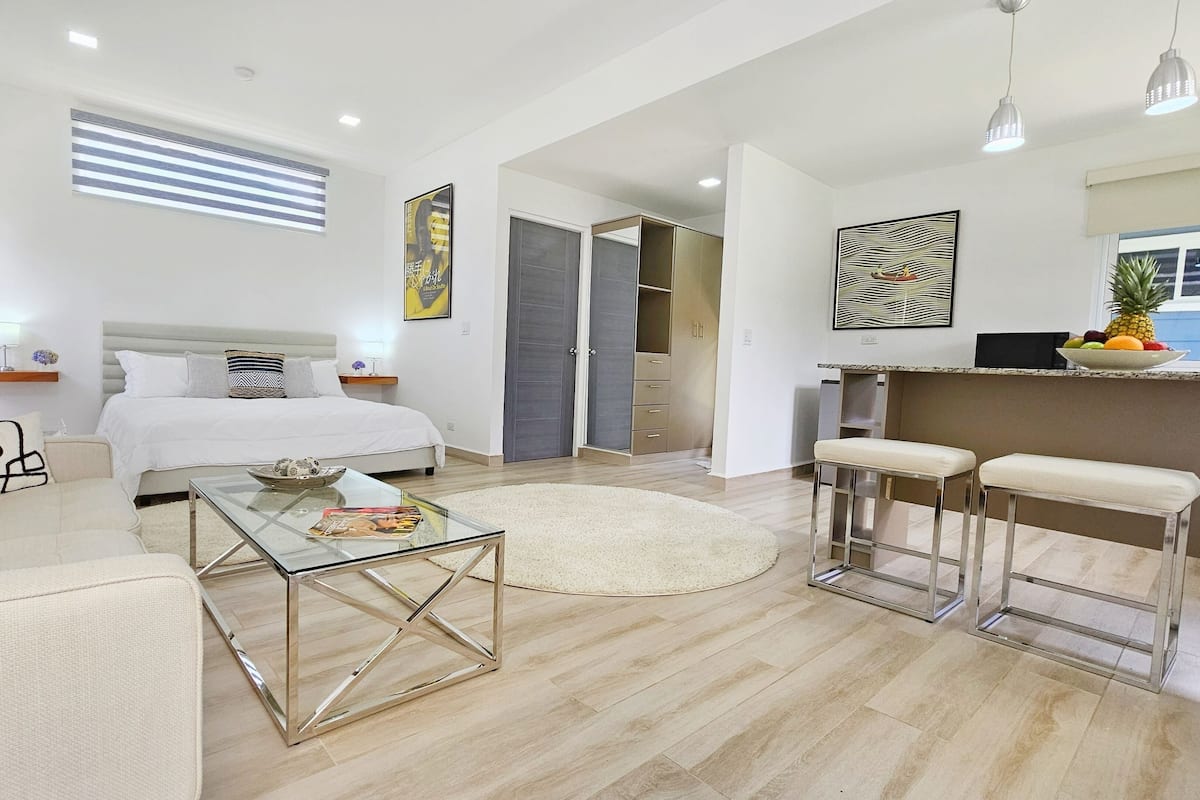A modern, well-lit bedroom with a large bed, bedside tables, and a glass coffee table.