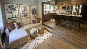 A cozy living room with a sofa, a coffee table, and a rug. Adjacent is a kitchen with wooden cabinets, a microwave, and a refrigerator. - Welcome to Brooks Run - A 1920s Cabin in Beautiful Brown County, Indiana (Nashville)