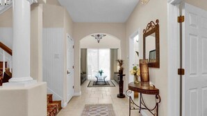 A hallway with a patterned rug, a console table with decorative items, and a mirror on the wall. - Magical Memories 5 BR Spacious Pool/Spa Home (Kissimmee)