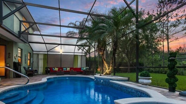 A swimming pool with a glass ceiling, surrounded by outdoor seating and greenery. - Magical Memories 5 BR Spacious Pool/Spa Home (Kissimmee)