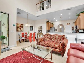 A spacious living room with a red sofa, a glass coffee table, and a dining area with red chairs.