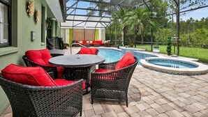 A covered outdoor area with a pool, wicker furniture, and a view of the surrounding greenery. - Magical Memories 5 BR Spacious Pool/Spa Home (Kissimmee)