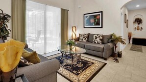 A living room with a sofa, a coffee table, and a dining area with chairs. - Magical Memories 5 BR Spacious Pool/Spa Home (Kissimmee)
