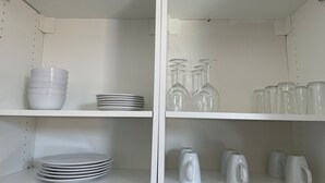Eine Küche mit weißen Regalen, auf denen weiße Schüsseln, Teller, Weingläser und Teekannen stehen.