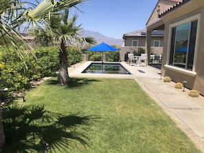 A backyard with a swimming pool, a palm tree, and a patio area with outdoor furniture.