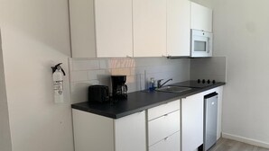 Una cocina compacta con armarios blancos, microondas, cafetera y lavavajillas.