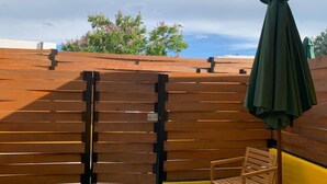 Una cerca de madera con un portón, una silla de madera y un paraguas verde.