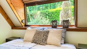 Un dormitorio con un ventanal grande, una cama con almohada estampada y dos jarrones decorativos en el alféizar.