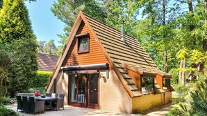Un pequeño edificio de forma triangular con techo inclinado, puerta de entrada de vidrio y un patio con mesa y sillas.