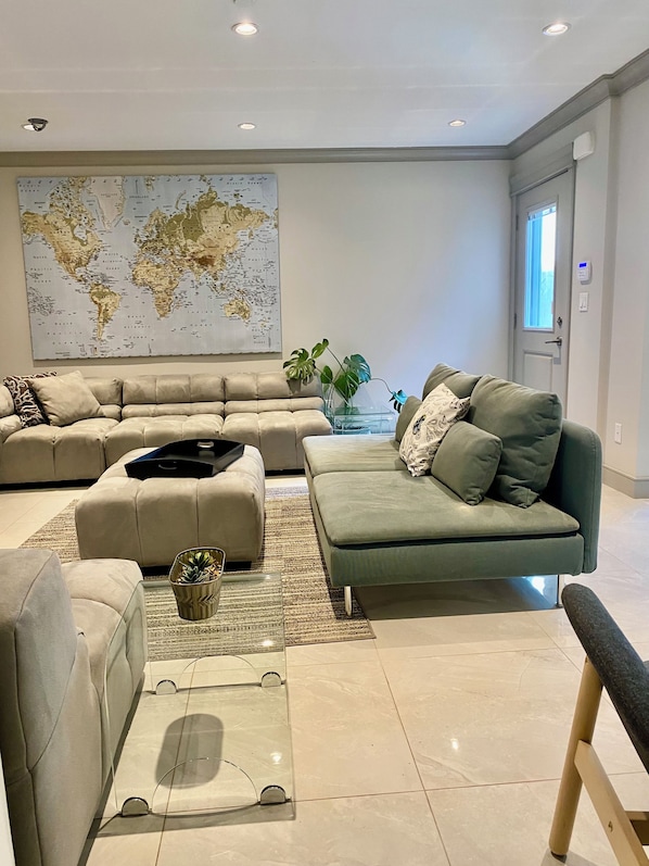 Un salon moderne avec un canapé d’angle, un fauteuil vert, une table basse et une carte du monde accrochée au mur.