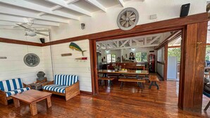 A spacious living area with wooden flooring, a blue and white striped sofa, a wooden coffee table, and a dining table with benches. A ceiling fan and a decorative wheel are visible. - Beachfront Villa – Just Steps from the Sand, Your Ocean Escape Awaits (Guanacaste Province)