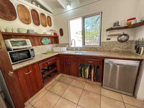 A kitchen with wooden cabinets, a stainless steel dishwasher, a microwave, and a sink. - Beachfront Villa – Just Steps from the Sand, Your Ocean Escape Awaits (Guanacaste Province)