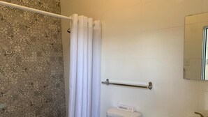 A bathroom with a patterned tile wall, a white toilet, a white sink, and a shower curtain. - Villa acogedora dentro del hospital Auxilio Mutuo 106 (San Juan)