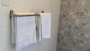 A bathroom with two white towels hanging on a metal towel rack. The wall has a patterned tile design. - Villa acogedora dentro del hospital Auxilio Mutuo 106 (San Juan)