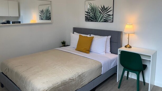 A bedroom with a bed, a desk, a chair, a lamp, and two framed pictures on the wall. - Villa acogedora dentro del hospital Auxilio Mutuo 106 (San Juan)