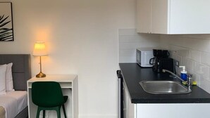 A compact kitchen with a sink, a microwave, and a coffee maker. There is a small dining area with a chair and a table. - Villa acogedora dentro del hospital Auxilio Mutuo 106 (San Juan)