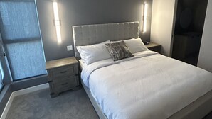 Ein modernes Schlafzimmer mit einem großen Bett, Nachttischen und Blick ins Freie.
