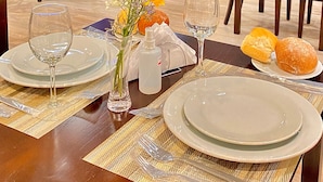 Un coin repas avec une table dressée pour deux personnes, un téléviseur fixé au mur et un canapé en arrière-plan.