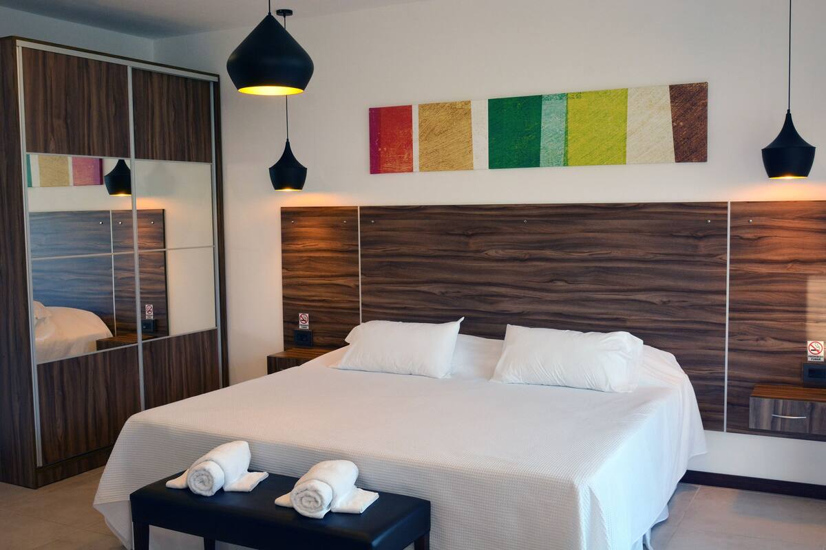 Une chambre d’hôtel moderne avec un grand lit, une tête de lit en bois et un nuancier fixé au mur.