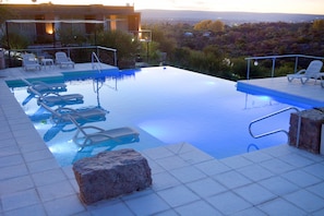 Una piscina infinita con sillas de descanso, un elemento decorativo de piedra y vistas a un paisaje lejano.