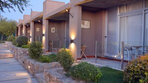 Une rangée de chambres d’hôtel, chacune dotée d’un balcon privé, de murs en pierre et d’un espace extérieur aménagé pour s’asseoir.