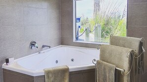 A modern bathroom with a freestanding bathtub, a towel rack with towels, and a window with a view of greenery. - Kaka Point Luxury Spa Accommodation (Kaka Point)