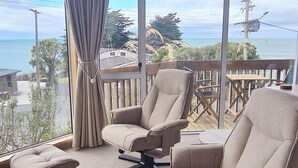 A balcony with a view of the sea, featuring two beige armchairs and a matching ottoman. - Kaka Point Luxury Spa Accommodation (Kaka Point)