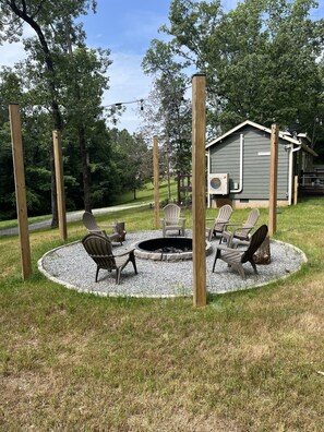 Ein runder Außenbereich mit Adirondack-Stühlen, einem Feuerkorb und einer Holzterrasse.