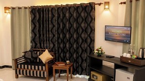 A living room with a sofa, a small table, a television, a mini-fridge, and a decorative wall panel.