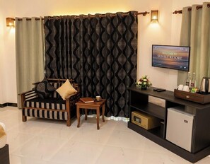 A living room with a sofa, a small table, a television, a mini-fridge, and a decorative wall panel. - Sunshine Resort and Spa (Sigiriya)