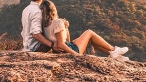 A couple sitting on a rocky outcrop overlooking a mountainous landscape.